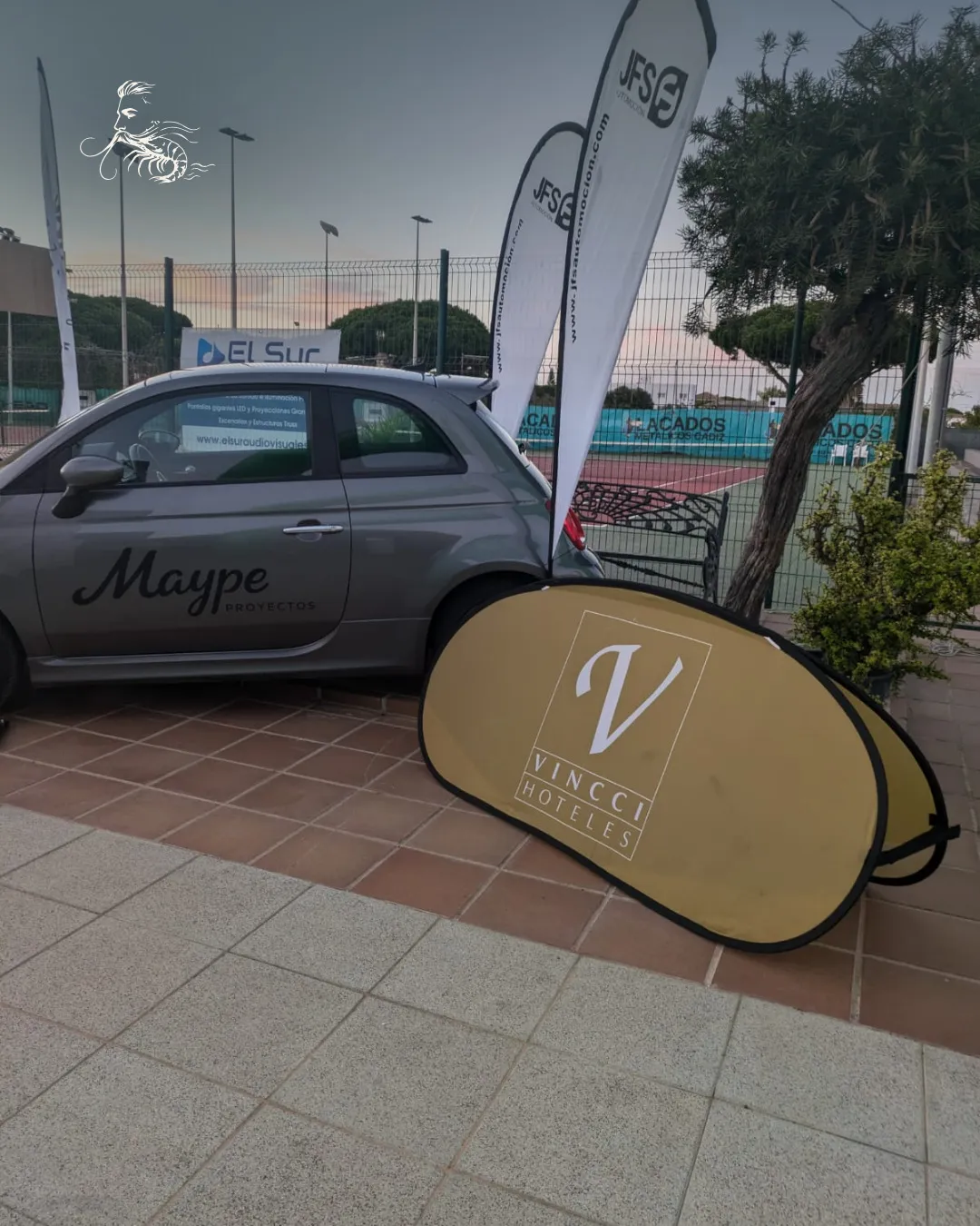 Coche y banderolas de patrocinadores junto a las pistas del Club La Barrosa durante el torneo